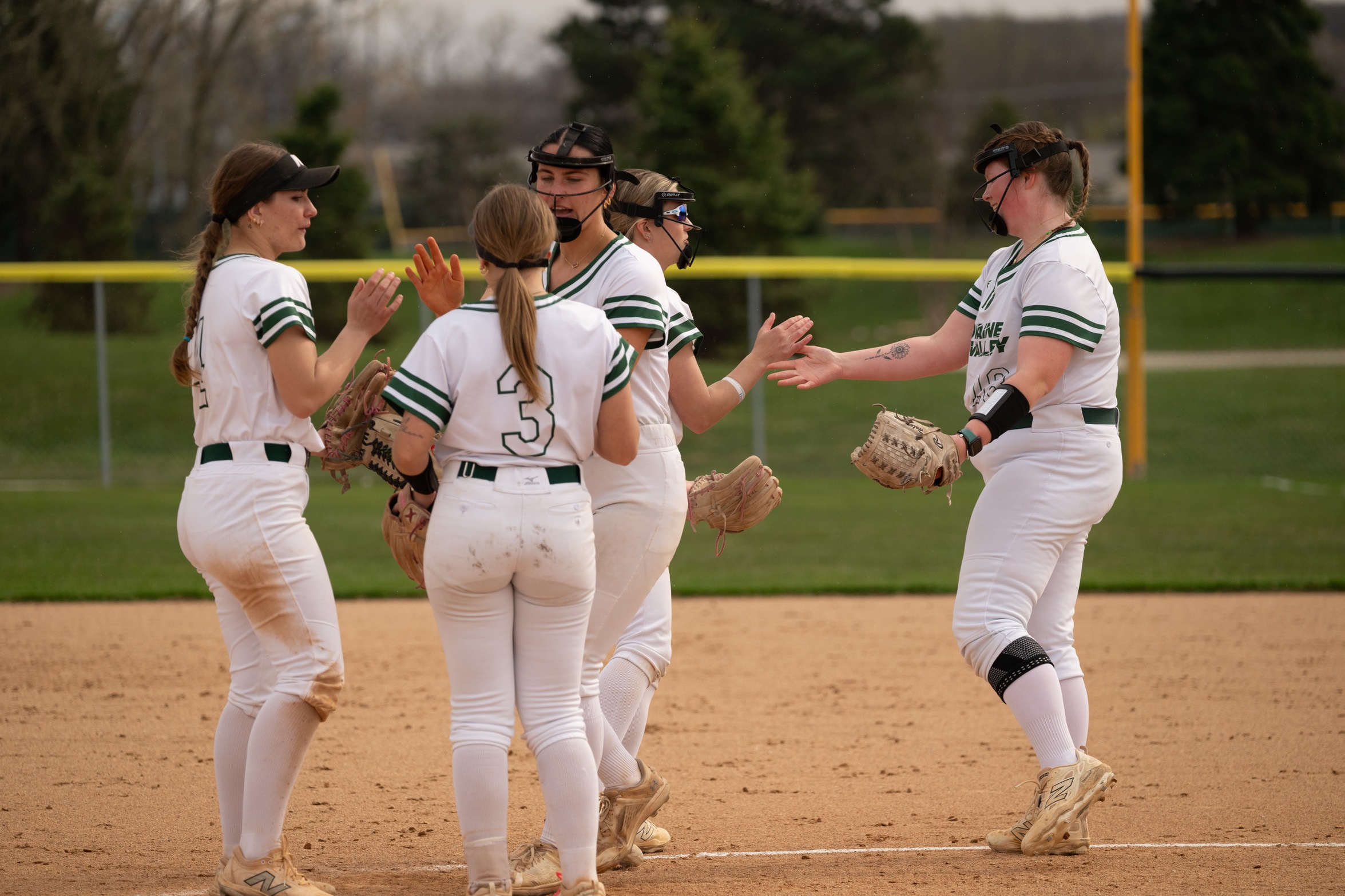 Moraine Valley softball players high five each other in the infield.